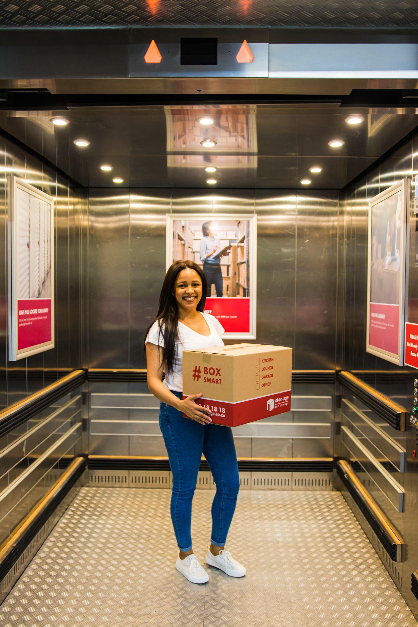Woman standing in elevator while holding a Stor-Age box.
